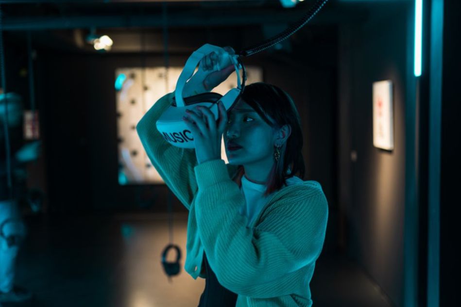 Besucherin, die VR-Brille mit der Aufschrift "MUSIC" aufsetzt, in der Ausstellung im MOMEM